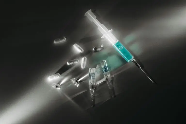 Syringe and medicine capsules illuminated in a dark, dramatic setting, emphasizing medical themes.